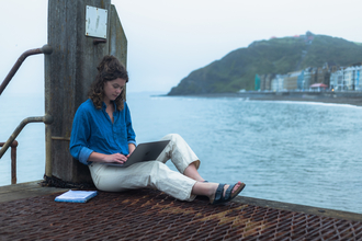 Freya Johns sat on a pier writing on her laptop.
