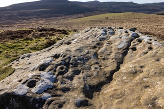An ancient rock carving. Hollows and grooves known as cup and ring marks can be seen on a large swathe of stone