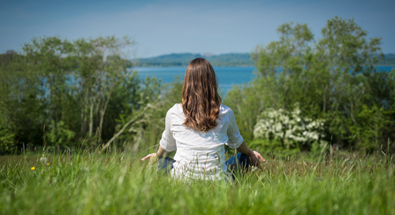 Woman meditating in a field, overlooking a river