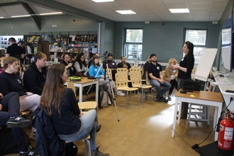 a group of people gathered indoors watching a speaker present. 