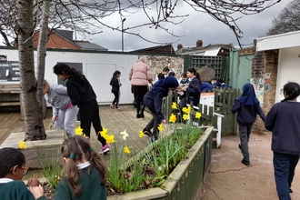 School kids play around a planter with daffodils growing. 