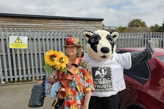 Woman holding sunflowers stands next to a person in a badger costume. 