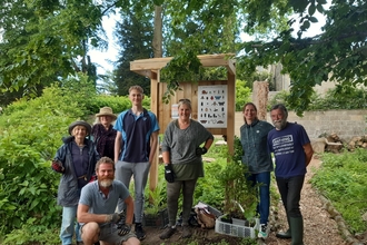 volunteers stand in front of a sign in a community garden