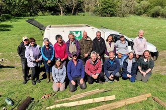 A group of volunteers pose in front of a van with grass and woodland in the background