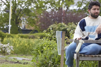 Man sits on a bench in a community garden. 