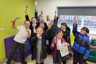 School kids holding garden tools in the air. 