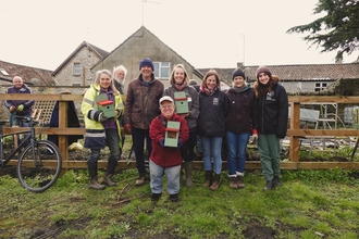 A group of volunteers stand outside with a garden space in the background. 