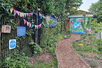 A newly planted orchard with a path running through the centre and a bright mural in the background. 