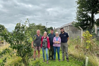 A group of people stand together in a garden among trees and plants. 