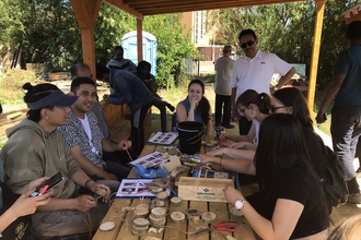 A group of people sit around a wooden table doing craft activities with pieces of wood. 