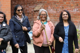 Four women smiling in a back garden holding gardening tools. 