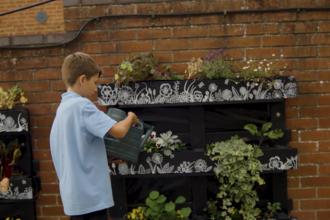 Boy in school uniform waters plants in a repurposed crate planters