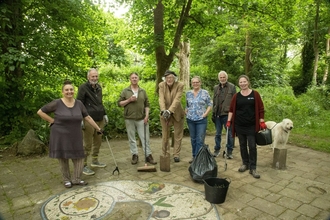 A group volunteers with litterpicking equipment gather in a wooded area