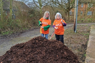 Two volunteers stand with a pile of compost 