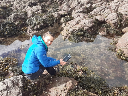 Mary kneeling by a rockpool with ipad. 