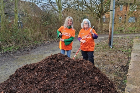 Two volunteers with a pile of wood chip. 