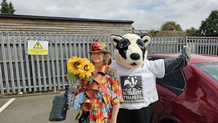 Woman holding sunflowers stands next to a person in a badger costume. 