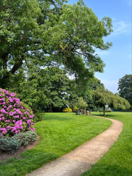 A path runsa through a park with trees and flowers on the left of the path. 