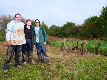 Three young people in muddy clothes in a green area. 