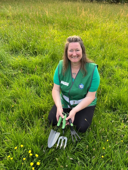 Woman sitting on the grass holding gardening tools