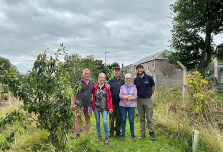 Group of people stand together in a community garden. 