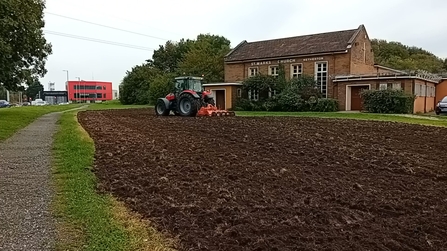 A tractor ploughs a grass area in front of a church.