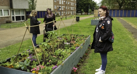 three people standing around a raised bed filled with flowers. 