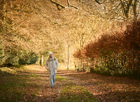 A woman walking in autumn colours, wearing a wooly hat and scarf