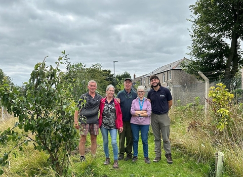 A group of people stand together in a garden among trees and plants. 