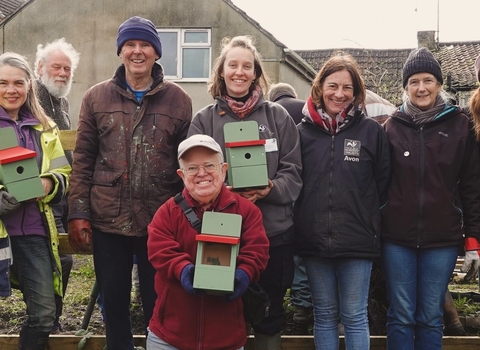 Volunteers pose with bird boxes in a community garden.