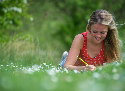 Lady in a meadow writing in a journal - smiling